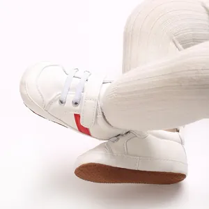 Vue rapprochée de chaussures de marche bébé à semelle souple, bande rouge et velcro
