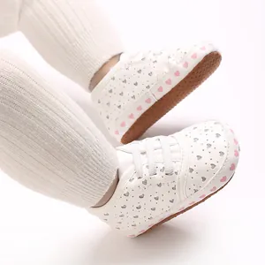 Detailed view of white baby sneakers with pink heart patterns and non-slip soft soles.