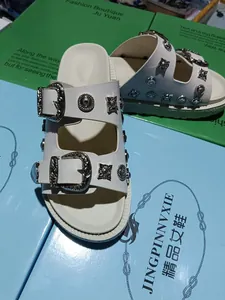 Close-up of white platform slides for women with ornate silver buckles and metal studs.