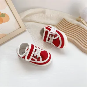 Red baby canvas sneakers with velcro straps and white soles on a minimalist white setup