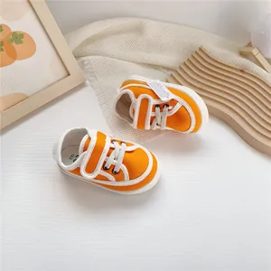 Top view of vibrant orange baby canvas shoes with velcro straps and soft white soles