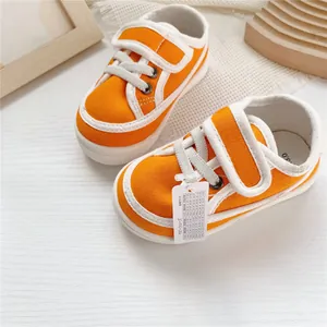 Detail view of orange baby canvas shoes featuring a soft sole and size hangtag.