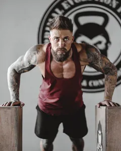 Gros plan d'un homme musclé portant un débardeur de fitness bordeaux dans une salle de sport.