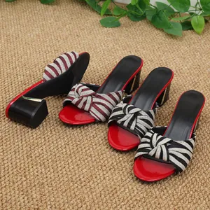 Eleganti pantofole da donna con tacco alto e fiocco a righe su un tappeto intrecciato