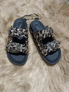 Detalle de sandalias de leopardo con hebillas metálicas decoradas y tachuelas en alfombra de piel.