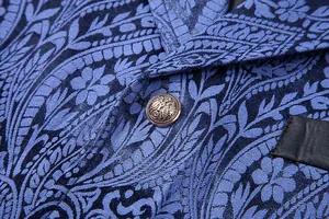 Close-up of blue paisley jacquard fabric and antique crest button on men's suit vest.
