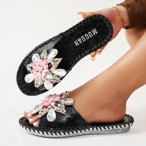 Vue détaillée de claquettes noires élégantes avec fleur en strass et semelle tressée.