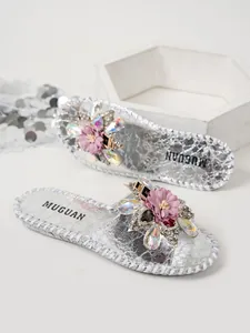 Gros plan de mules plates argentées avec des détails élégants de fleurs en strass