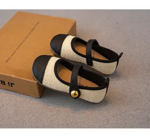 Nahaufnahme cremefarbener Tweed-Kinderschuhe mit eleganten schwarzen Lederakzenten