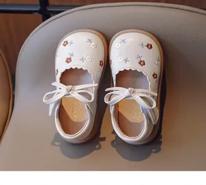 Détail de chaussures en cuir crème pour fillettes avec broderies florales et jolis nœuds