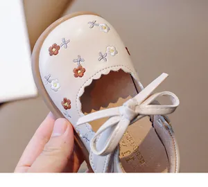 Gros plan de chaussures bébé fille avec broderie florale et nœud décoratif.