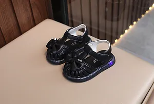 Detailaufnahme schwarzer Kleinkinder-Sandalen mit Schleife und leuchtender LED-Sohle.