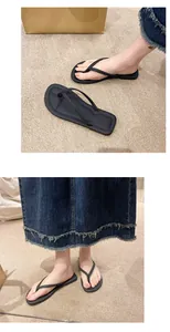 Schwarze flache Zehentrenner-Sandalen für Damen, getragen mit Jeansrock auf Teppich