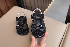 Detailansicht von schwarzen Kleinkind Mädchen-Sandalen mit schicker Schleife und 'min' Logo