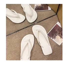 Detaillierte Nahaufnahme von weißen minimalistischen flachen Damen-Zehentrennern auf Teppich