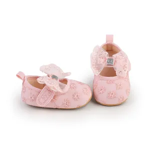 Close-up detail of pink baby girl walking shoes with lace bow and floral embroidery.