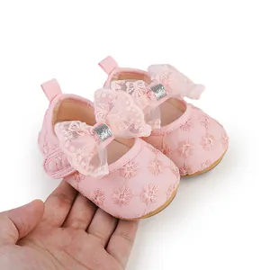Close-up detail of pink lace baby shoes featuring floral embroidery and a glittery bow