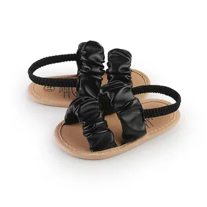Detailed view of black faux leather ruffled baby sandals with soft tan soles for infants