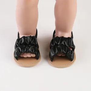 Close-up of black ruffled infant summer sandals with tan soles on a doll's feet.