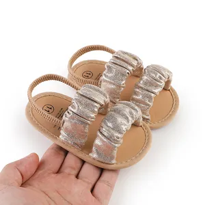 Macro detail view of shiny champagne gold cloud baby sandals with soft soles being held