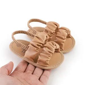 Detail view of brown ruffled cloud baby sandals with soft soles held in hand for scale