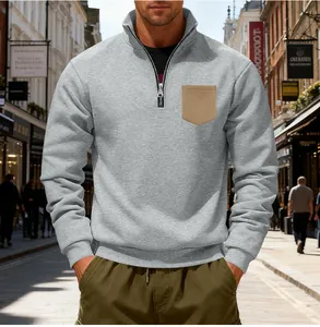 Man wearing a grey half-zip fleece sweatshirt with a khaki pocket in an urban street.