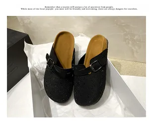 Close-up detail of black rhinestone mules with buckle strap in a white display box.