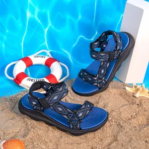 Sandali da spiaggia blu per bambini con cinturini a motivi e suola antiscivolo su sabbia.