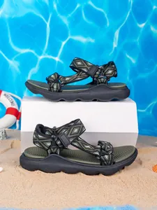 Vista laterale di sandali sportivi verdi da bambino sulla sabbia con sfondo mare estivo