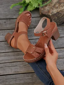 Braune High-Heel-Sandalen mit Peeptoe-Design, Lochmustern und Goldnieten auf Holzdeck