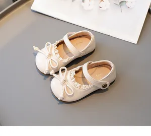 Chaussures Mary Jane crème pour enfants avec nœud et dentelle sur fond gris élégant.