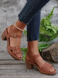 Braune lasergeschnittene High-Heel-Sandalen mit Nieten und Perlenfußkettchen am Modell