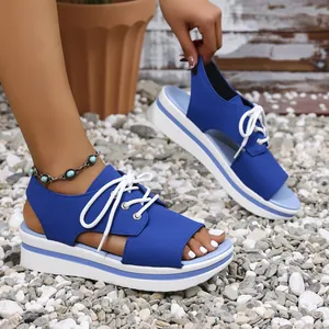 Close-up of blue platform sandals with white laces and open-toe design on gravel