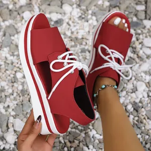 Detailed close-up of red platform sandals featuring white laces on a natural gravel surface