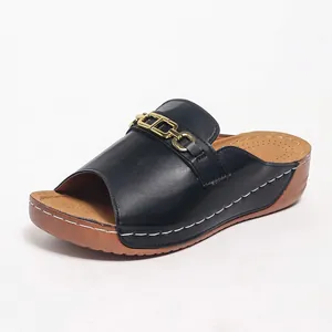 Dettaglio di eleganti ciabatte nere da donna con zeppa e catena dorata decorativa