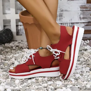 Detailed side view of women's red lace-up platform sandals on a natural gravel surface