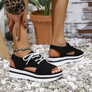 Detailed side view of black peep-toe platform sandals with white laces on pebble ground