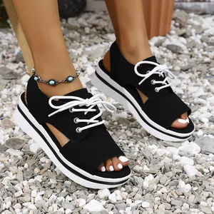 Close-up of black platform sandals with white laces and peep-toe design on pebbles