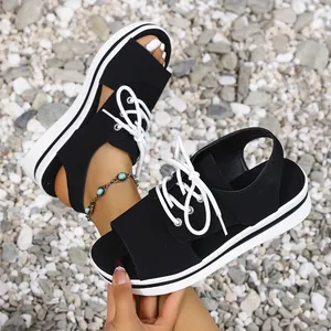 Close-up view of women's black platform sandals with white laces on a gravel background.