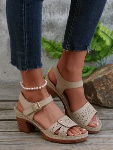 Detailansicht beige Leder-Sandalen mit Durchbruchmuster und Nieten auf Holzboden