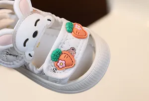 Gros plan d'une sandale blanche pour bébé avec de mignons décors de lapin et de carotte.