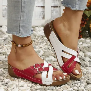 Detail view of red and white wedge sandals with metal buckles on pebble ground