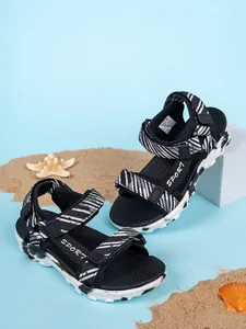 Primer plano de sandalias de rayas para niños con logo SPORT en un ambiente playero