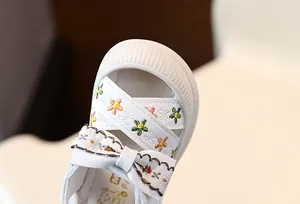 Gros plan détaillé de sandales de princesse blanches pour bébé avec broderies et nœud papillon