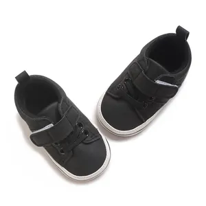 Close-up top view of black baby pre-walker shoes featuring soft white soles and velcro straps.