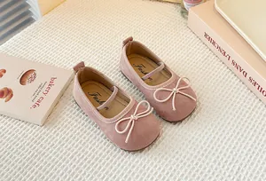 Close-up of pink girls' Mary Jane shoes with bow detail resting on white textured fabric