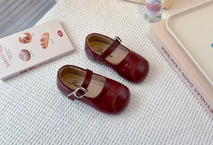 Detail of burgundy girls' Mary Jane shoes with silver buckle on a textured background.