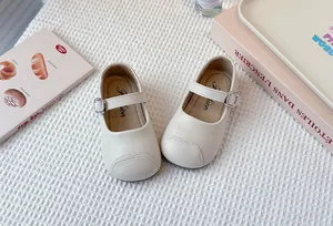 Detail of cream Mary Jane shoes for girls with buckle strap on white textured background