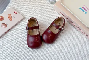Close-up of burgundy children's Mary Jane shoes with soft soles on a white textured background