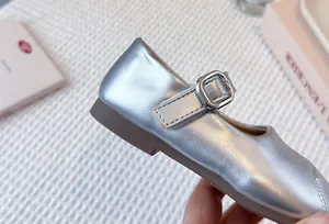 Detail of metallic silver girls Mary Jane shoe showing the buckle strap and leather texture
